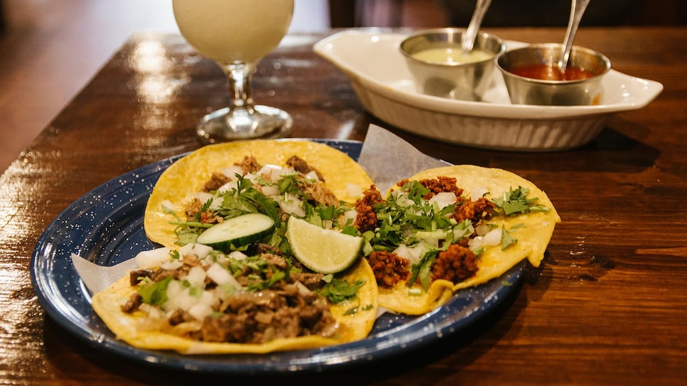 Une assiette avec trois tacos dedans.
