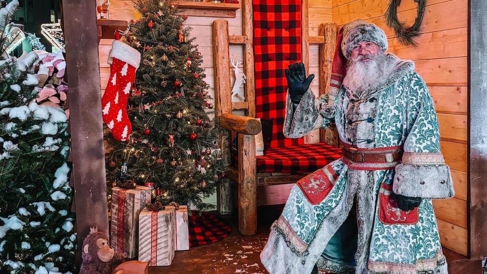 Le Père Noël salue les gens devant sa maisonnette en bois. 