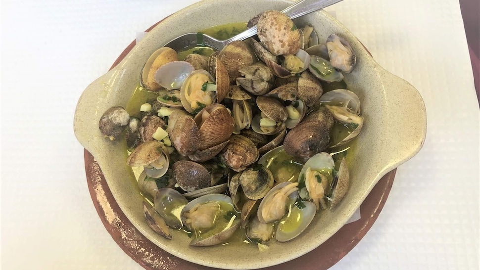 Des palourdes dans un plat de service avec de l'ail, de l'huile d'olive et de la coriandre.