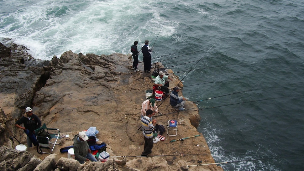 Plusieurs hommes portugais qui pêchent assis sur un rocher au bord de la mer.