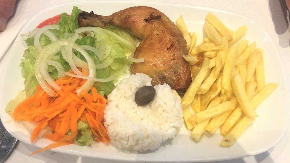 Une assiette contenant une cuisse de poulet, des frites, du riz et de la salade.