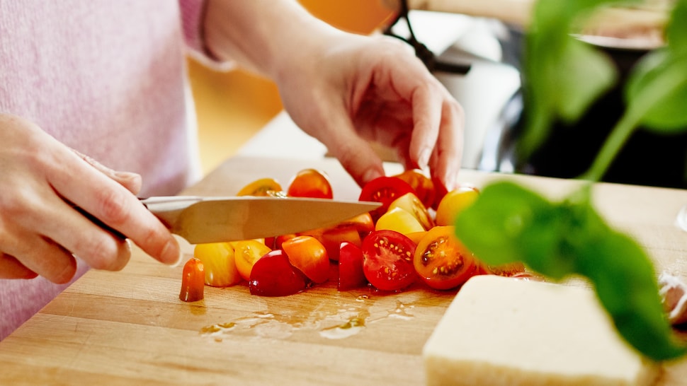 Une femme qui tranche des tomates cerises sur une planche à découper en bois.