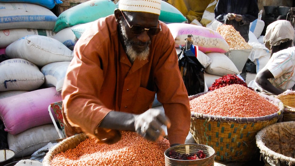 Vendeur dans un marché sénégalais devant des paniers remplis de produits.
