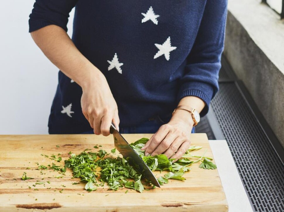Une personne coupe du persil italien en utilisant un couteau de cuisine sur une planche à découper. 

