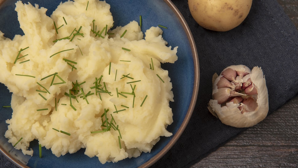 Pommes de terre écrasées et ciboulette dans un bol, gousse d'ail et une patate.