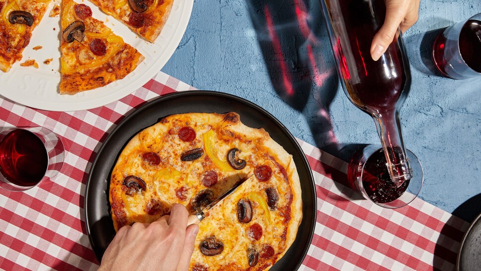 Deux pizzas garnies de pepperonis et de champignons avec des verres de vin rouge.