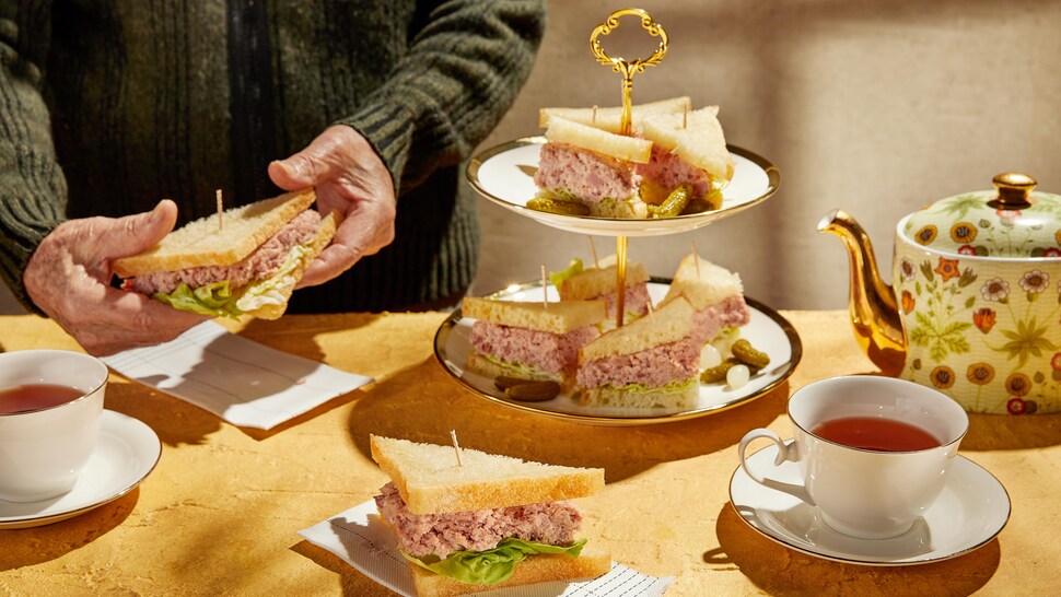 Plusieurs sandwichs au jambon coupés en triangles dans un joli présentoir servis avec du thé.