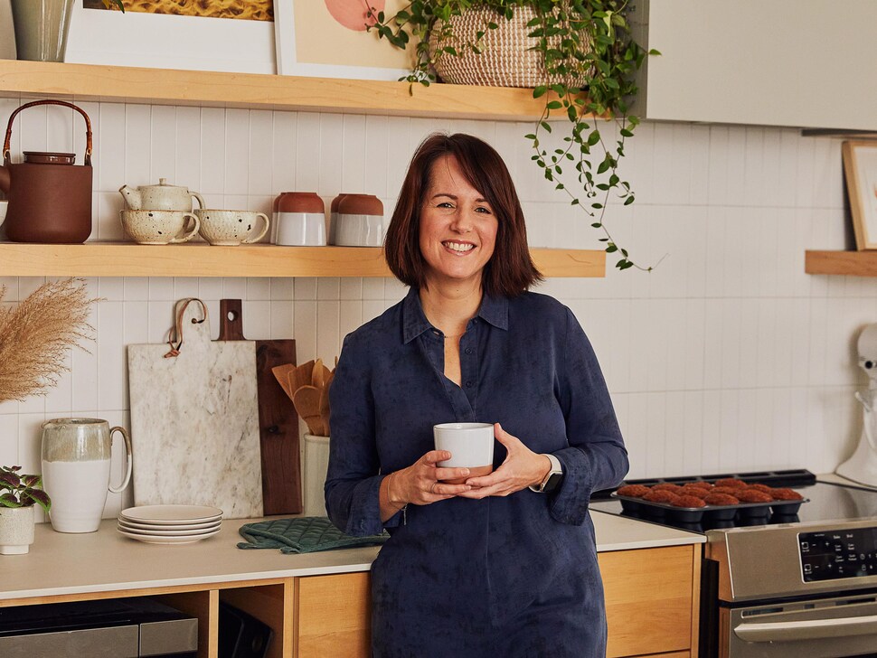 La nutritionniste Geneviève O’Gleman est dans une cuisine un thé à la main et des muffins aux bananes sont sur le comptoir.
