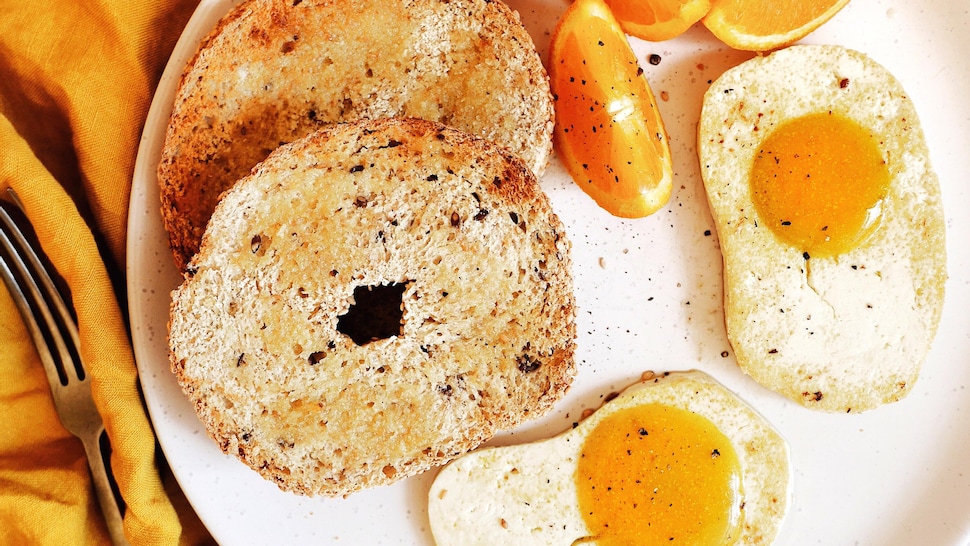 Une assiette contenant des bagels, des quartiers d'orange et deux œufs miroir sans œufs.