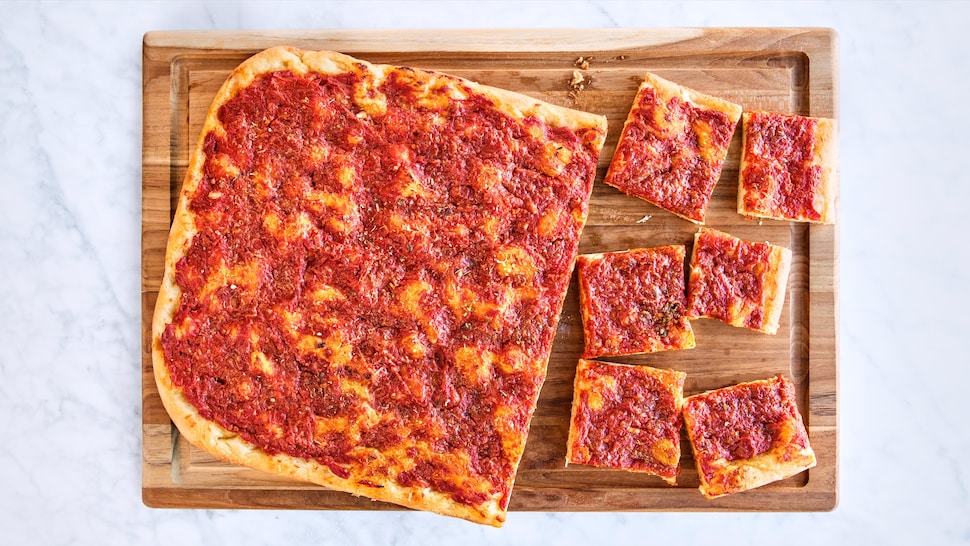 Une pizza froide sur une planche à découper avec certains morceaux de coupés.