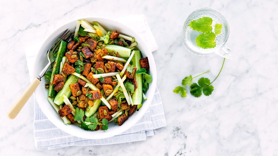 Un bol de salade mesclun avec des juliennes de pomme verte, du concombre en quartiers et du tempeh au miel-cari.