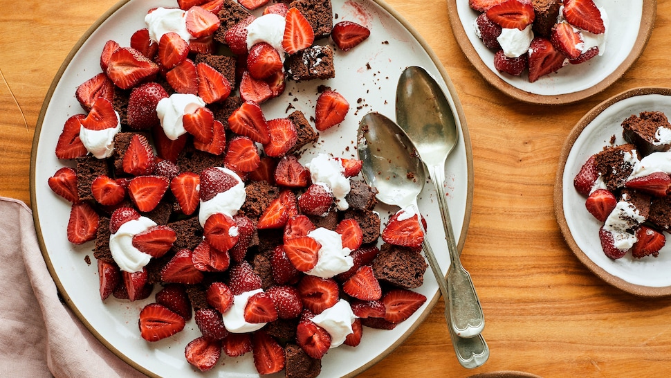 Sur une table en bois, est déposé une grande et deux petites assiettes contenant de la bagatelle choco-café aux fraises. 