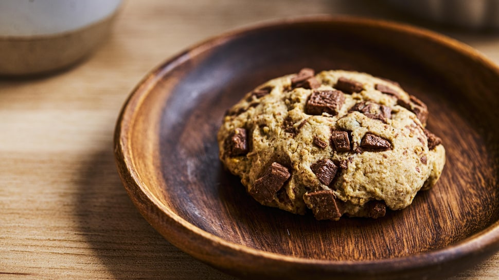 Un biscuit aux brisures de chocolat dans une assiette de bois.