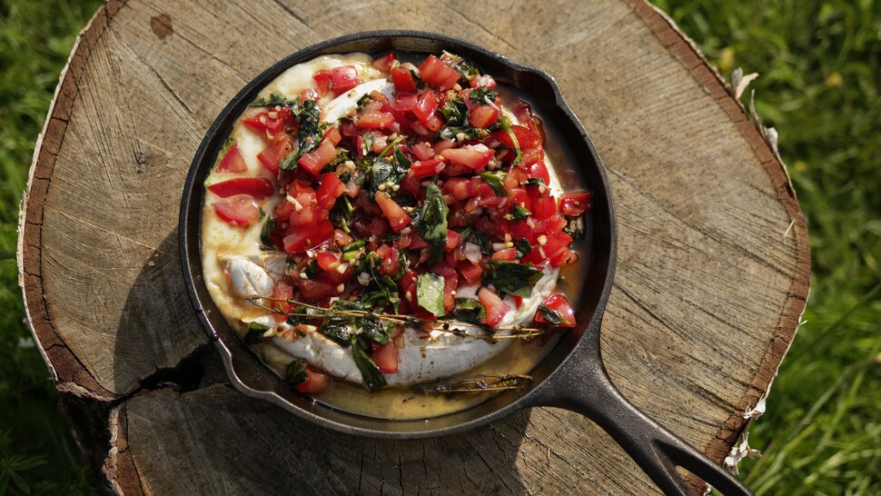 Une meule de fromage brie fondant garni de bruschetta, dans une poêle.