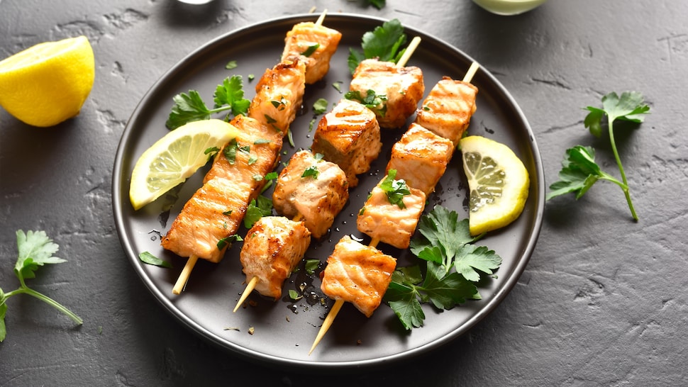 Trois brochettes de saumon dans une assiette noire.