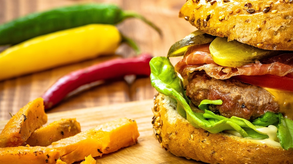 Un burger de boeuf au cheddar et frites de patate douce sur une planche de bois.