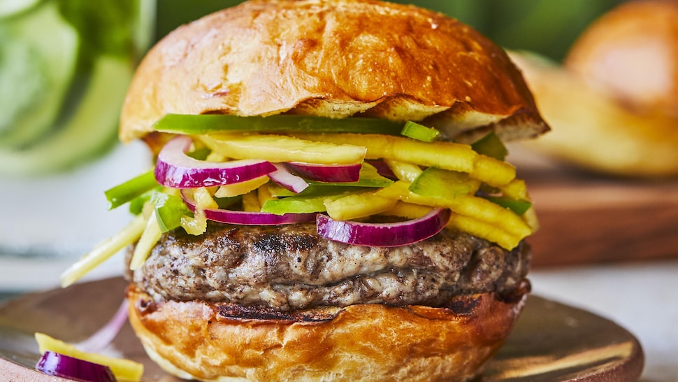 Un burger à la jamaïcaine garni de morceaux de mangue, de poivron vert et d'oignon rouge.