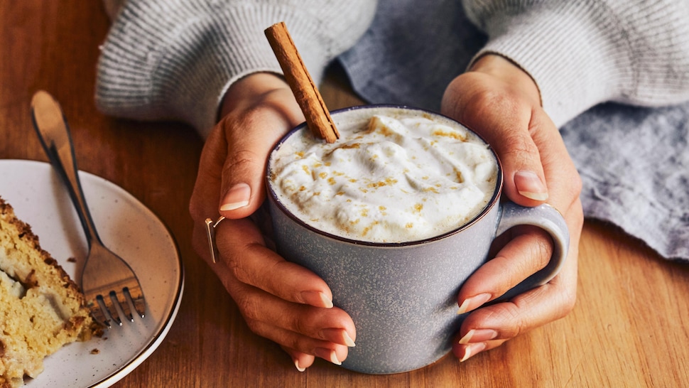Des mains qui tiennent une tasse remplie de café latté à la brioche à la cannelle.