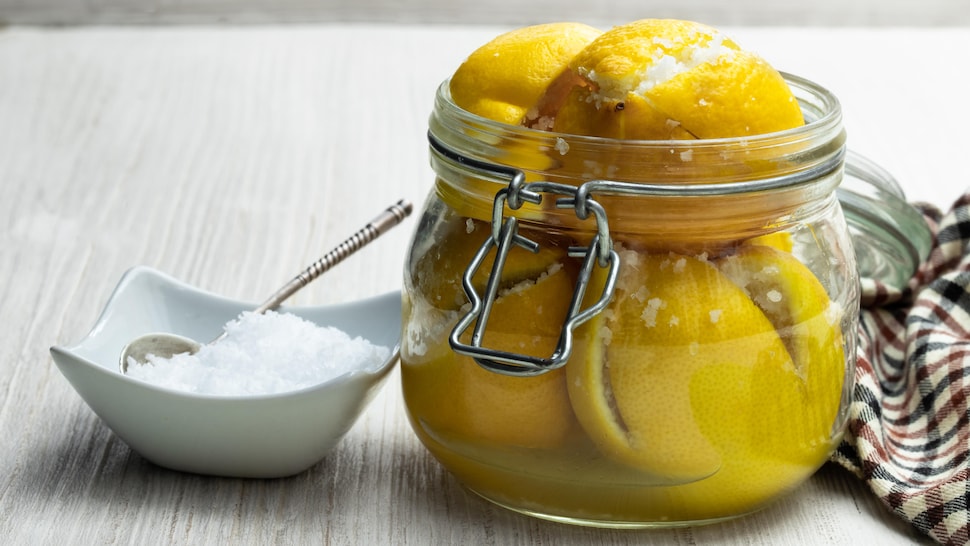 Des citrons confits dans un pot avec un petit bol rempli de gros sel à côté.