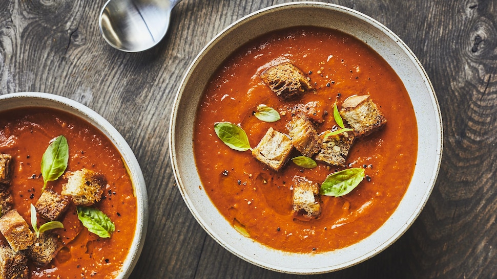 Deux bols blancs avec de la crème de tomates et des croûtons sur le dessus. 