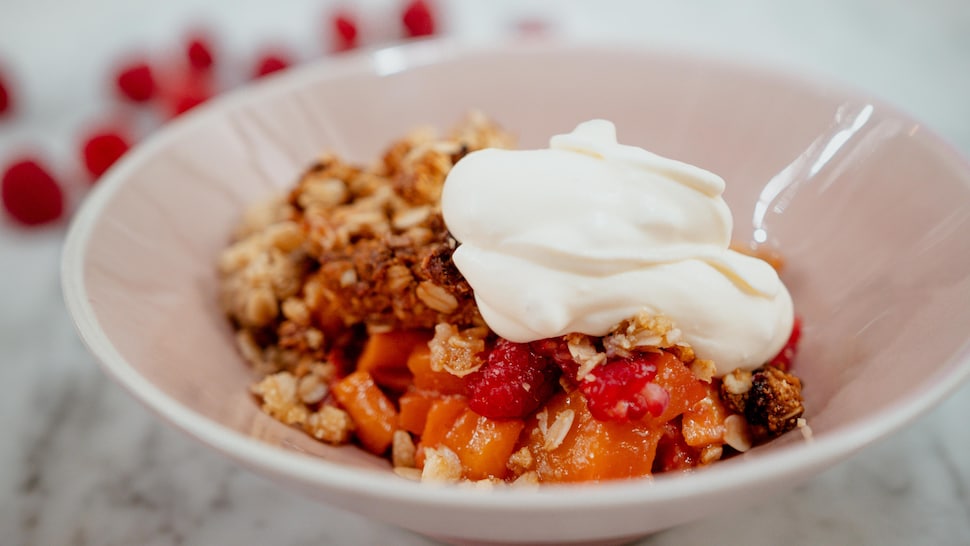 Un bol de croustade à la mangue et aux framboises garni de crème fouettée.