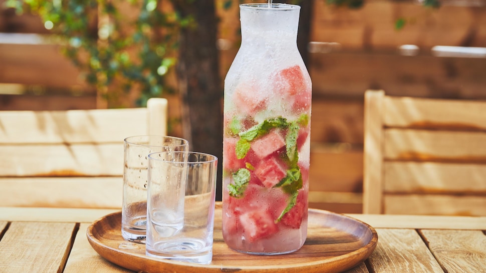 Une bouteille transparente en verre avec de l'eau pétillante au melon d'eau avec deux verres vides juste à côté. 