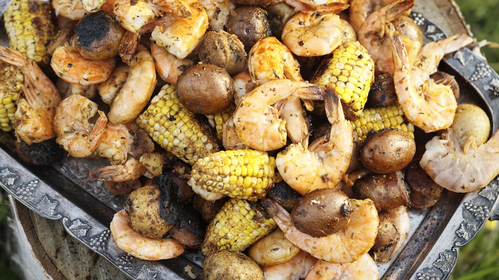 Un mélange de crevettes de morceaux de saucisses, de morceaux d'épis de maïs et de patates grelots grillés sur une plaque de cuisson à l'ancienne.