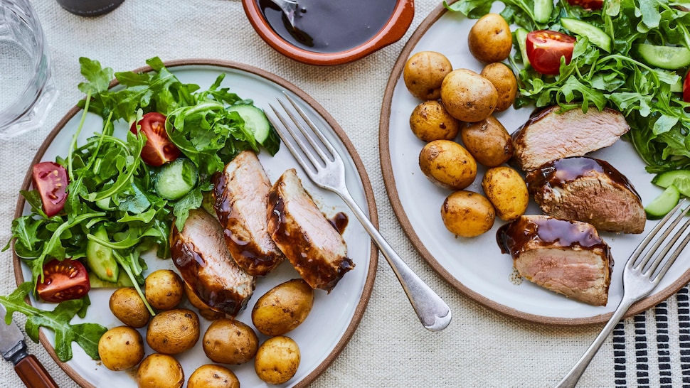 Deux assiettes de filet de porc tranché avec des pommes de terre grelots et une salade verte, accompagnées d’un petit pot de sauce. 