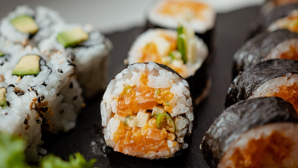 Des futomakis au saumon épicé sur un plateau à sushi.