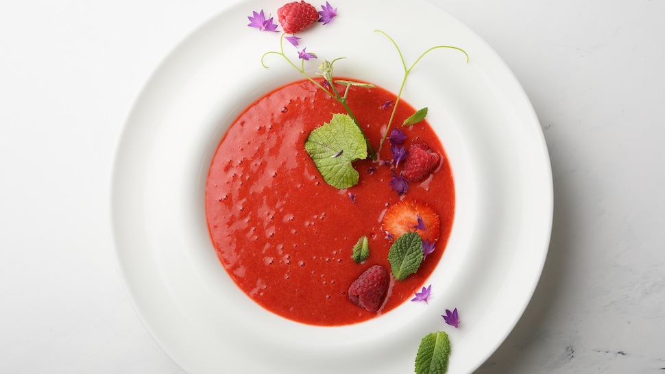 Un bol de gaspacho au melon d'eau et aux tomates garni de fraises et d'herbes fraîches.
