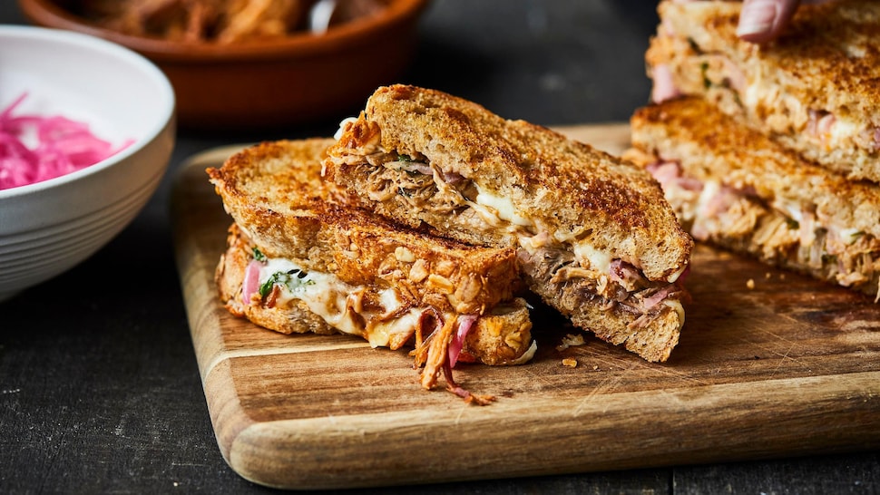 Deux grilled cheese au porc effiloché sur une planche de bois.