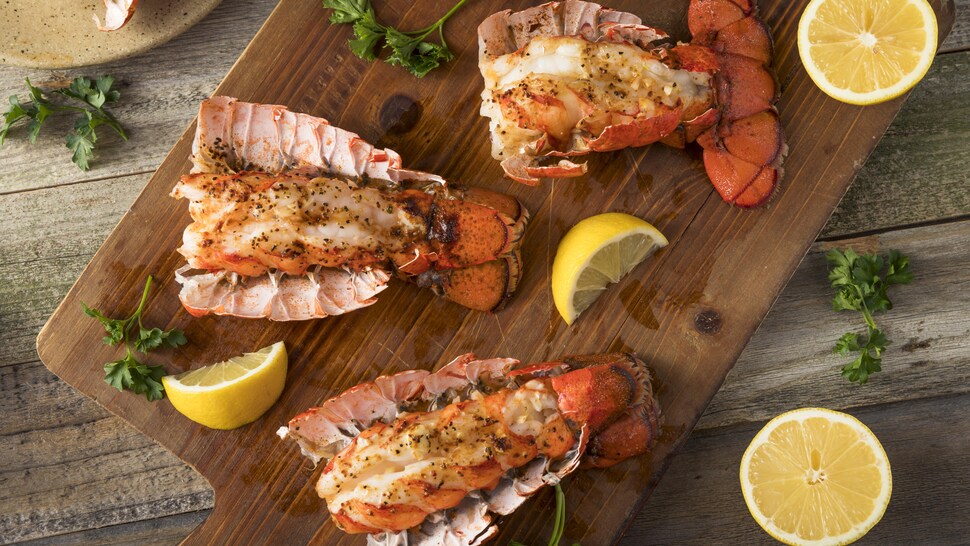 Trois queues de homard sur une planche à découper avec du citron et du persil.