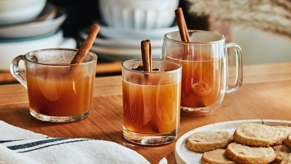 Sur une table est déposé trois verres contenant le jus de pomme chaud et une assiette de biscuits.