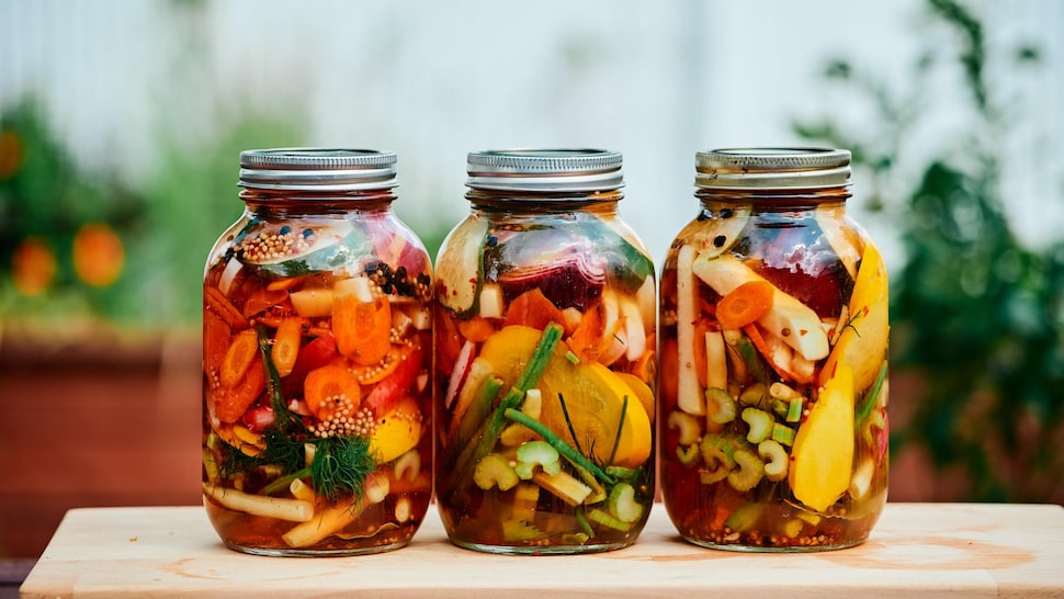 Trois pots masson avec des légumes marinés à l'intérieur.