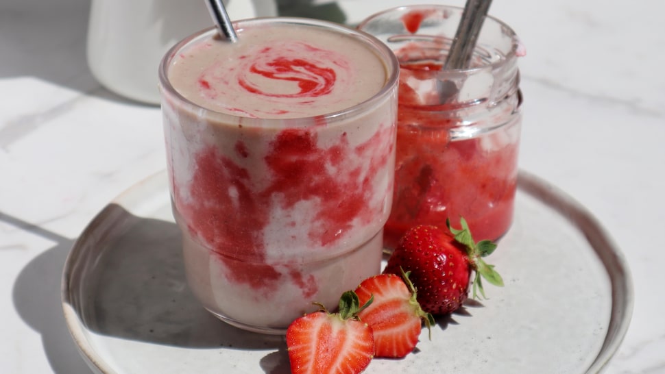 Un smoothie tourbillonnant de crème et de coulis de fraises dans un verre, à côté d'un pot de confiture de fraises.