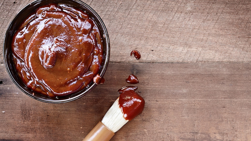 Un pot de sauce barbecue avec un pinceau dont le bout est recouvert de sauce.