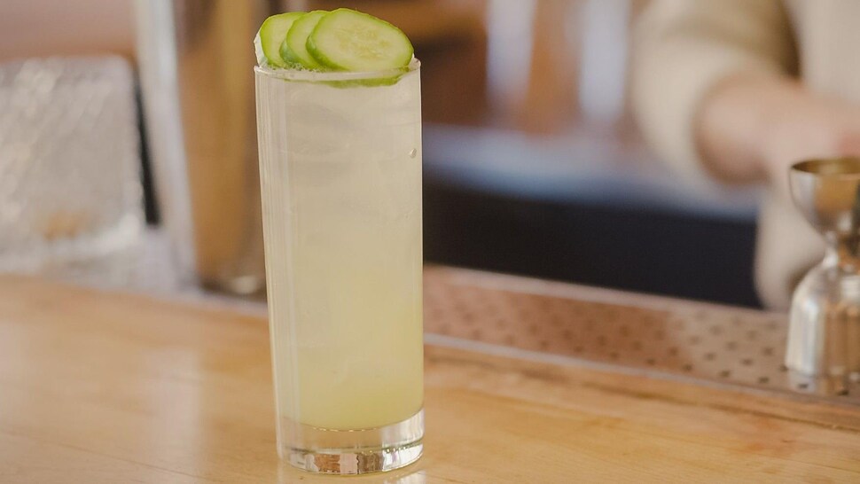 Un cocktail dans un verre avec trois rondelles de concombre en guise de décoration.