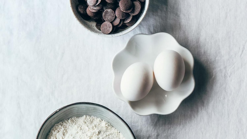 Les ingrédients principaux pour le moelleux au chocolat, dans des petits bols, dont du beurre, de la farine, des oeufs et des pastilles de chocolat.