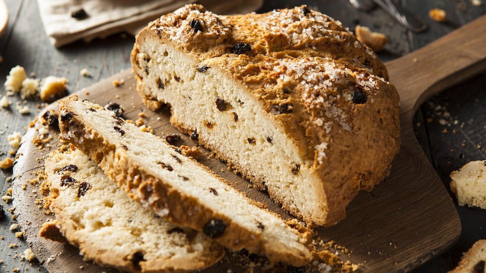 Une miche de pain au soda, parsemée de raisins secs et de gros sel, sur une planche à découper.