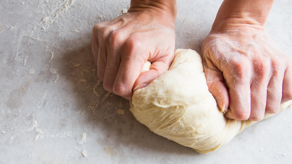Des mains qui pétrissent de la pâte à pizza.