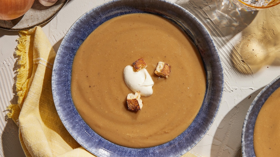 Potage garni de crème aux croûtes de parmesan et croûtons de baguette dans un bol.