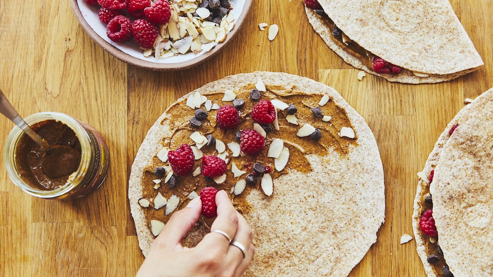 Une main en train de garnir une quesadilla déjeuner de framboises et de tartinade au chocolat. 