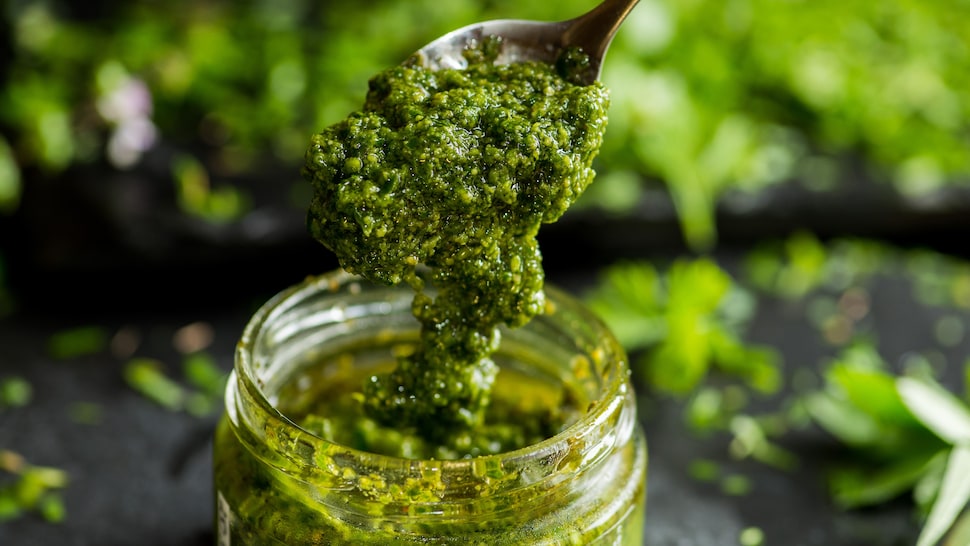 Une cuillère trempée dans un pot de pesto aux herbes.