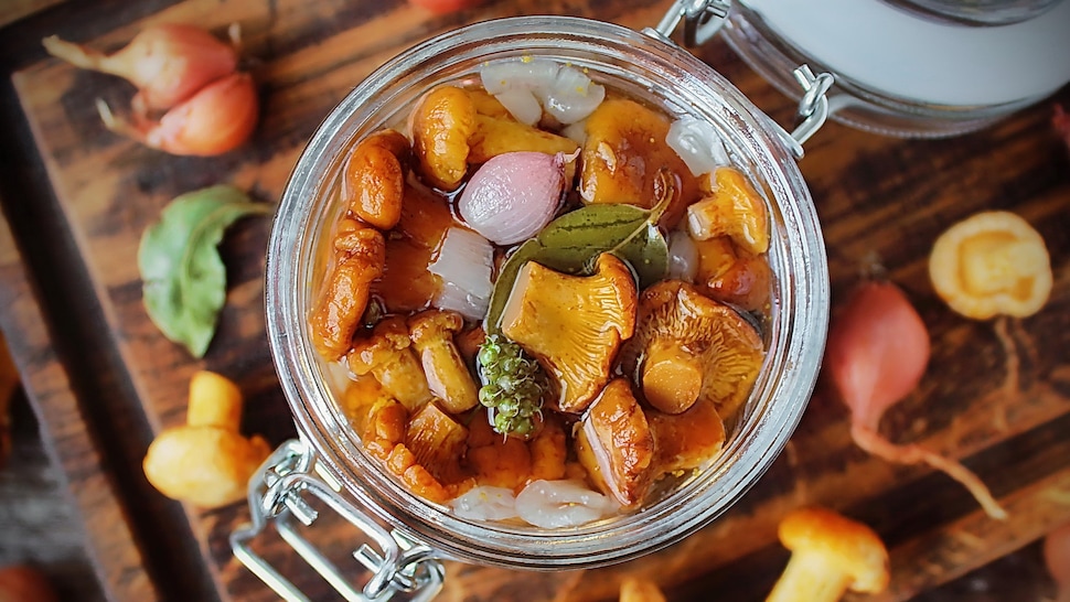 Des champignons marinés dans un bocal entouré de champignons et d'oignons.