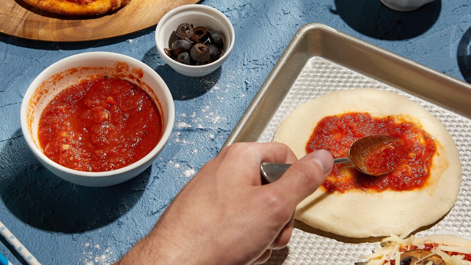 Un petit bol de sauce à pizza avec une pâte à pizza en train de se faire recouvrir de sauce.