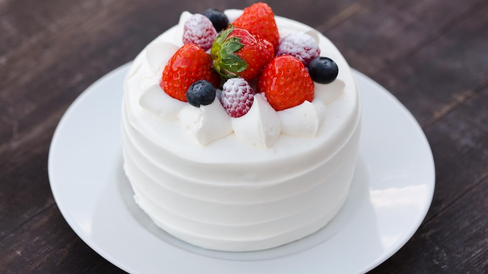 Un petit gâteau recouvert de crémage blanc et de petits fruits.