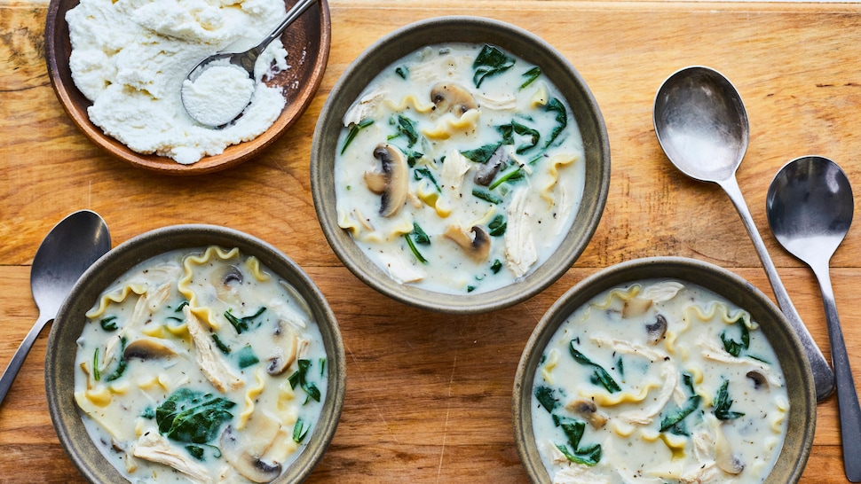 Trois bols de soupe-lasagne sur une table en bois accompagnés de ricotta.