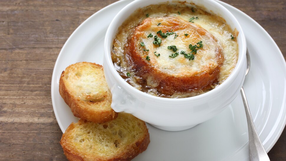 Une bol de soupe à l'oignon gratinée dans une assiette avec deux morceaux de pain.