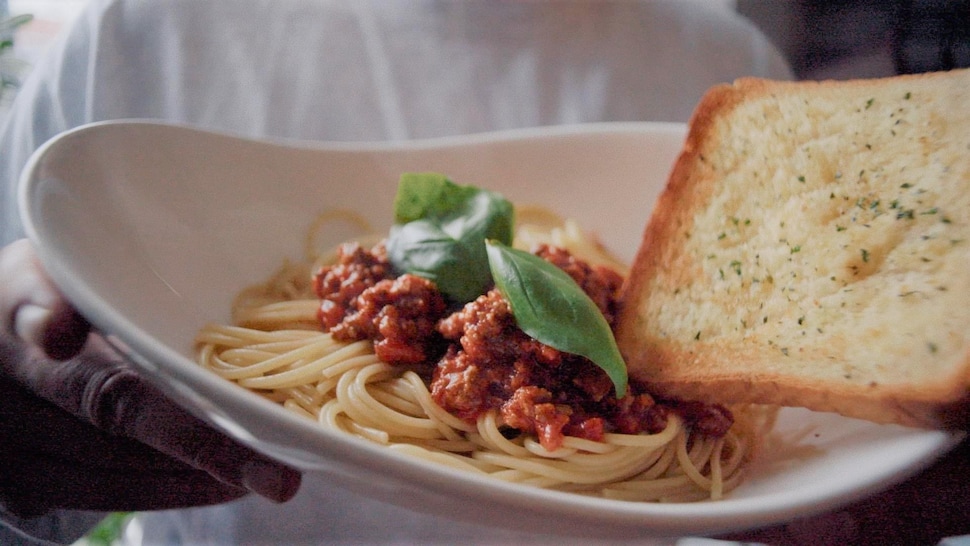Un bol de spaghetti, garni de sauce bolognaise et de basilic frais, accompagné d'une tranche de pain à l'ail.