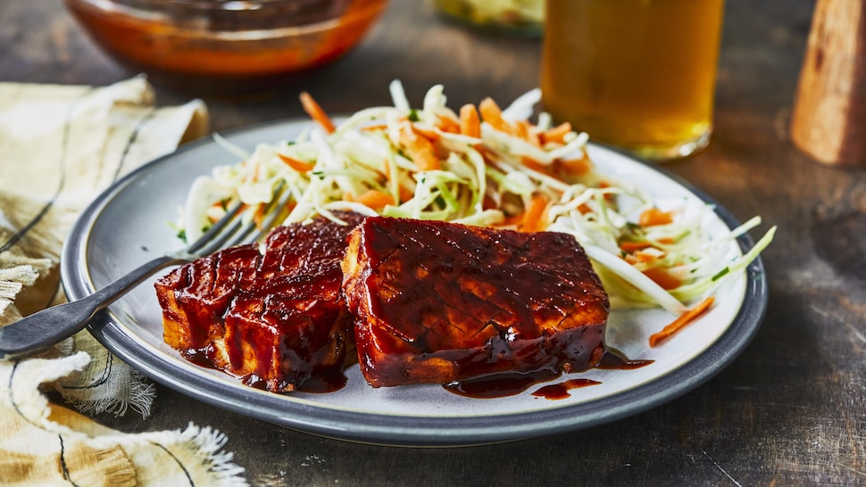 Du tofu grillé dans une assiette, accompagné de salade de chou et d’un verre de bière. 